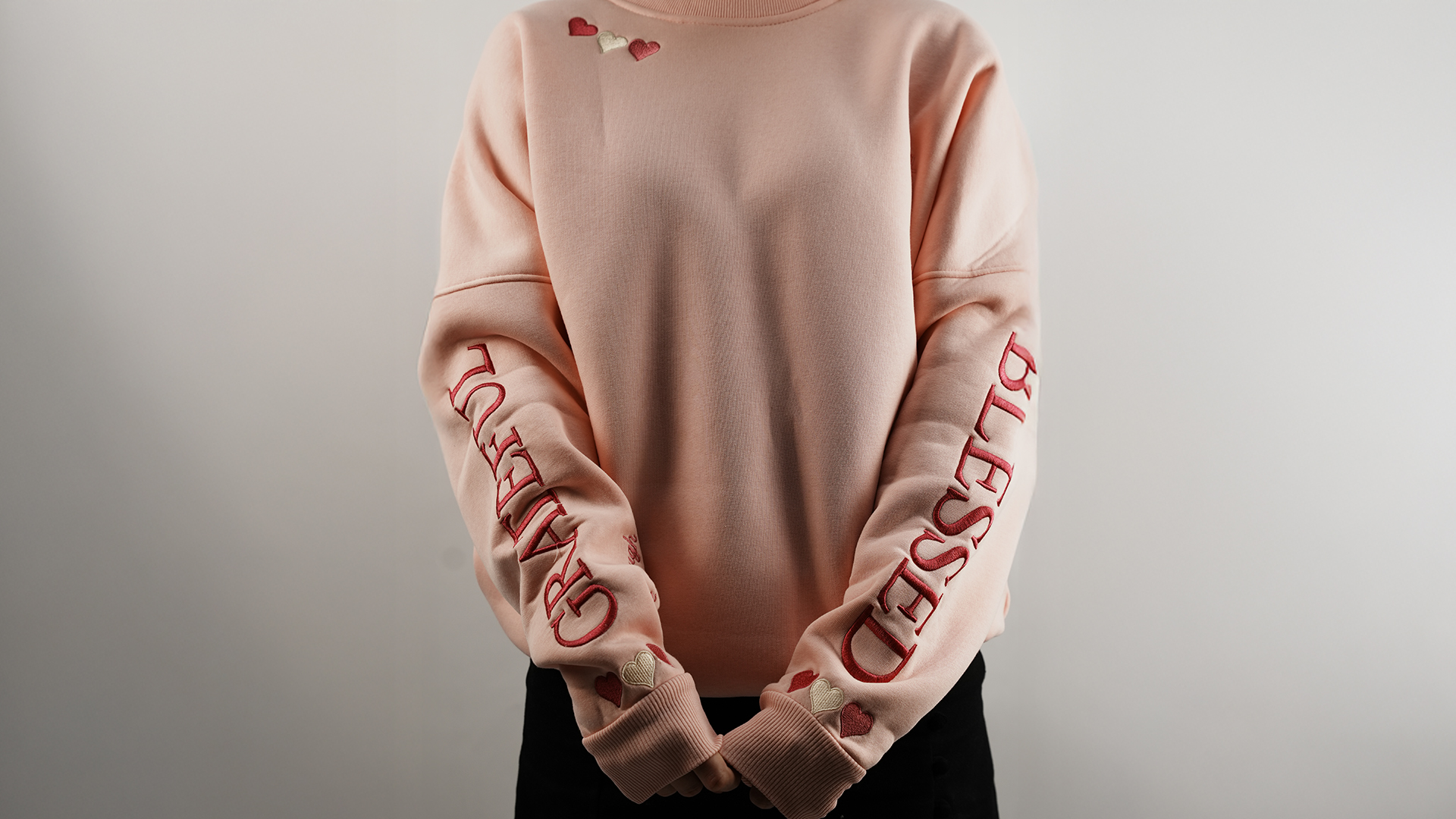 Pink sweatshirt with embroidered hearts and words “GRATEFUL” and “BLESSED” on sleeves
